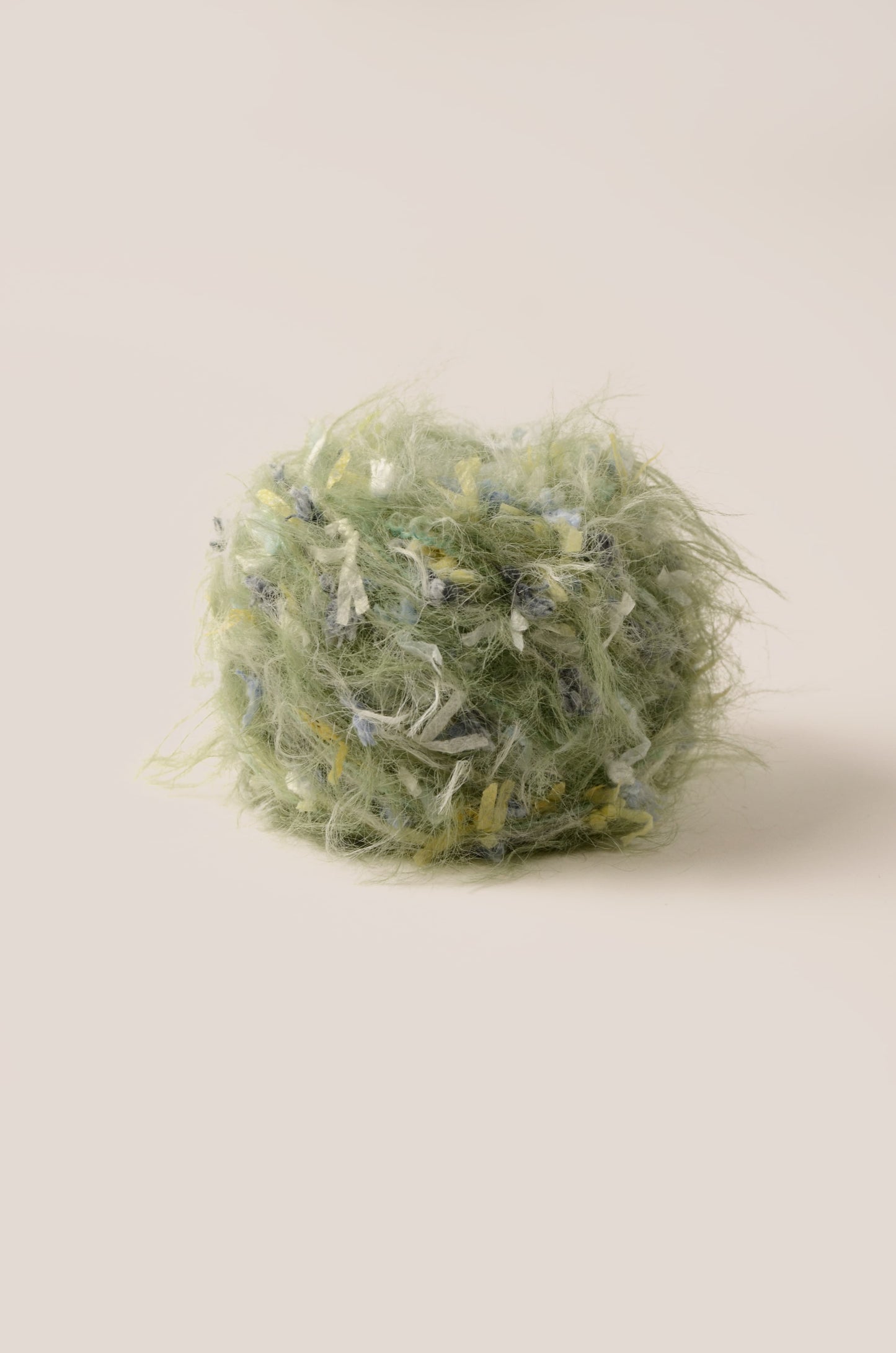 Lush Fern hand-blended yarn – muted grass green base with blue, yellow, and white threads, soft fluffy texture inspired by rainy meadows