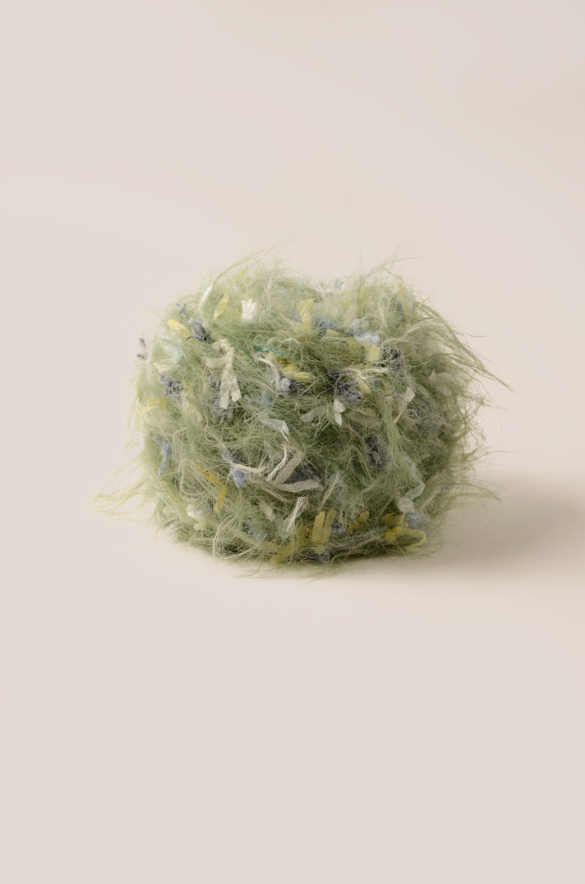 Lush Fern hand-blended yarn – muted grass green base with blue, yellow, and white threads, soft fluffy texture inspired by rainy meadows